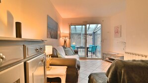 A cozy living room with a sofa, a small table, and a chair. There is a sliding glass door leading to a balcony with outdoor seating. - Stunning  villa for 4 people with WIFI, TV, terrace and pets allowed (Saint-denis-d'oléron)