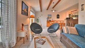 Ein modernes Wohnzimmer mit Sofa, zwei Sesseln, einem Couchtisch und einem Essbereich mit Tisch und Stühlen.