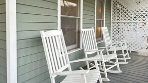 Une véranda avec des fauteuils à bascule blancs et une clôture en treillis.