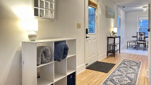 Un couloir avec une porte blanche, une petite table avec une lampe, un tapis bleu et un plancher en bois.