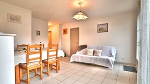 A small, well-lit room with a dining table and chairs, a sofa, and a bed.
