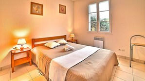 A bedroom with a bed, bedside tables, a radiator, a window, and a ceiling light fixture.