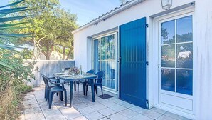 A patio with a table and chairs, a blue door, and a view of trees and a building.