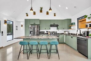 Une cuisine moderne avec des meubles de couleur verte, un îlot en marbre et trois tabourets de bar bleus.