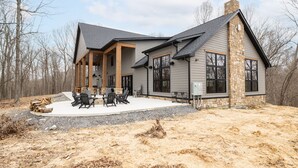 Een modern huis met een stenen schoorsteen, grote ramen en een terras met tuinmeubilair.
