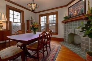A dining room with a wooden table and chairs, a chandelier, a fireplace, and large windows. - Central Charleston Craftsman (Charleston)