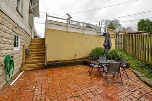 A patio with a brick floor, a table and chairs, and a wooden fence. - Central Charleston Craftsman (Charleston)