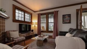 A cozy living room with a flat-screen TV, a fireplace, and a comfortable seating area with a couch and chairs. - Central Charleston Craftsman (Charleston)