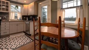 A kitchen with wooden cabinets, a dining table with chairs, and a patterned rug. - Central Charleston Craftsman (Charleston)