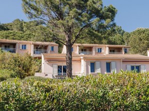A row of Mediterranean-style villas with terracotta roofs, surrounded by lush greenery and pine trees.