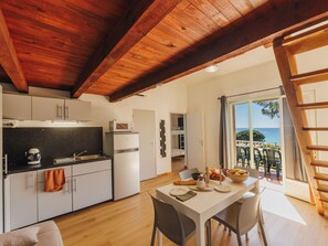 A compact kitchen with modern appliances, a dining area with a table set for two, and a balcony with a view of the sea.