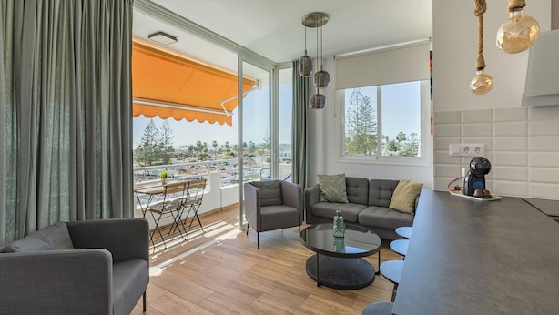 A modern living room with a sofa, chairs, a coffee table, and a balcony with an orange awning. - Stunning  villa for 4 guests with pool, WIFI, A/C, TV, terrace and pets allowed (Playa Del Ingles)