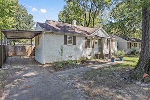A two-story house with a covered porch, a fenced yard, and a large tree.
