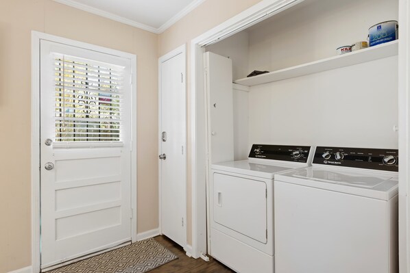 A laundry room with a white door, a window with blinds, and two white front-loading washing machines.