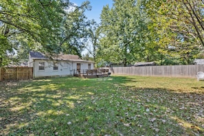A residential backyard with a house, a wooden deck, and a fenced area.
