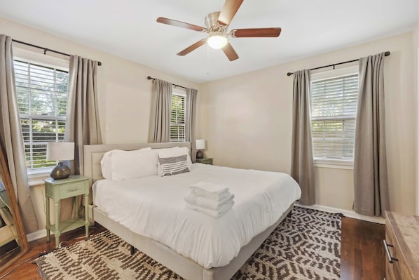 A bedroom with a bed, a nightstand, a lamp, a ceiling fan, and a window with blinds.