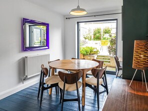 Un comedor con una mesa redonda de madera y sillas, un radiador blanco, un espejo con marco morado y vistas al exterior.