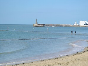 Una playa con un muelle y un faro al fondo.