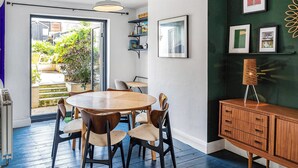 Zona pranzo con un tavolo rotondo in legno e sedie, un armadietto in legno scuro e una parete verde decorata con quadri.
