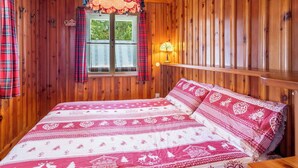A wooden room with a bed, plaid curtains, a window with a view, and a wall-mounted lamp. - Beautiful private villa for 9 guests with hot tub, WIFI, TV, balcony and pets allowed (Madesimo)