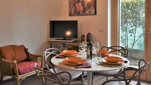 Een eetgedeelte met een ronde tafel gedekt voor vier personen, een televisie en een schilderij aan de muur.