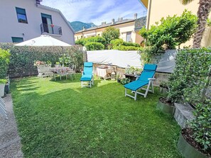 A well-maintained garden with two blue lounge chairs, a white table with chairs, and a white canopy.