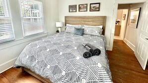 Un dormitorio con una colcha estampada, un cabecero de madera y una mesita de noche con una lámpara. Hay tres cuadros enmarcados en la pared sobre la cama.