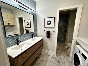 Un baño moderno con dos lavamanos, un espejo grande y una zona de ducha.