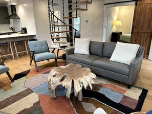Una sala de estar moderna con un sofá gris, una mesa de centro de madera y una escalera.