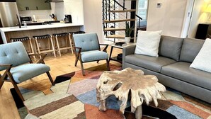Una sala de estar moderna con un sofá gris, dos sillones, una mesa de centro de madera y una alfombra colorida.