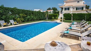 A swimming pool with lounge chairs and a sun umbrella, surrounded by greenery and a large house in the background. - Wonderful private villa for 10 guests with WIFI, A/C, private pool, TV and terrace (Albufeira)