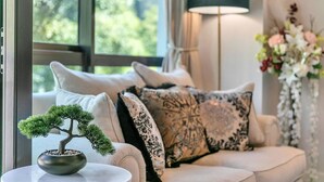 A cozy living room with a sofa, decorative pillows, a bonsai tree, a floor lamp, and a vase with flowers. - Viaduct`s Hidden Gem (Auckland)