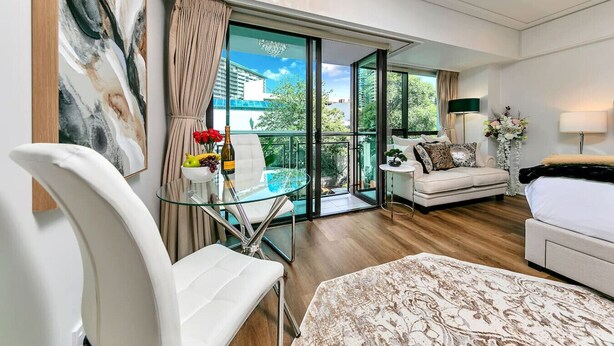 A modern hotel room with a glass table, a sofa, a bed, and a balcony with a view of buildings. - Viaduct`s Hidden Gem (Auckland)