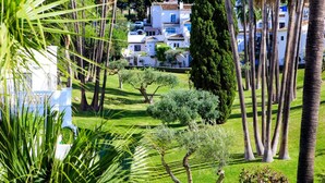 Une villa blanche, dotée d’un toit en tuiles, entourée d’une végétation luxuriante et de palmiers.
