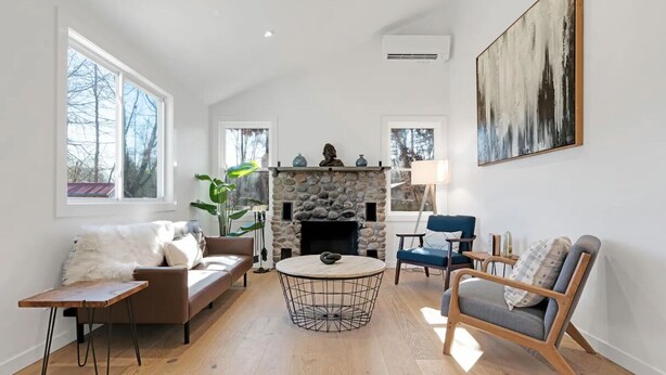 A living room with a stone fireplace, a round coffee table, a sofa, a chair, and a painting on the wall.