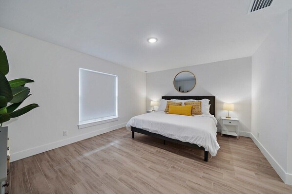 Une chambre à coucher avec un lit, des tables de chevet, un miroir et une fenêtre.