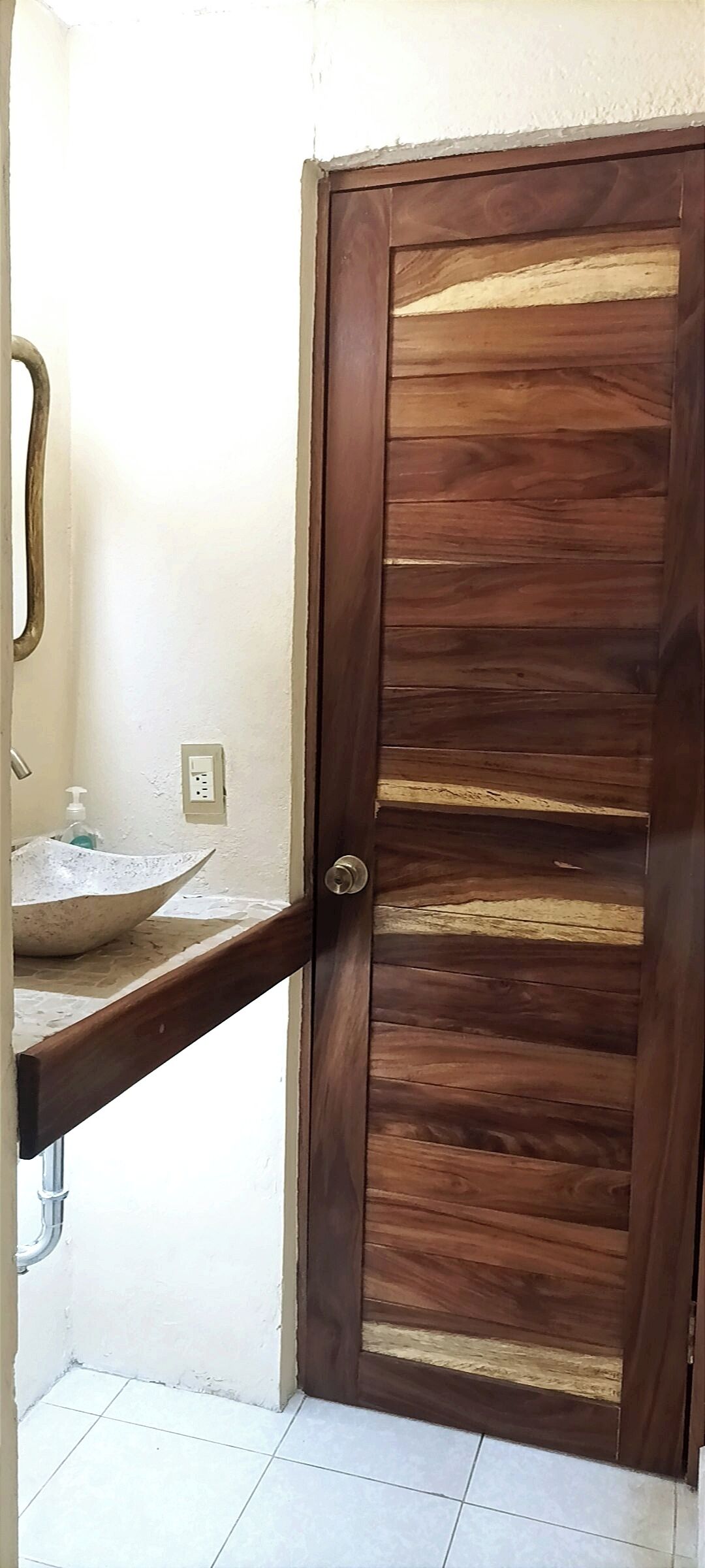 A wooden door with a unique design, a bathroom with a large sink, and a visible electrical outlet.
