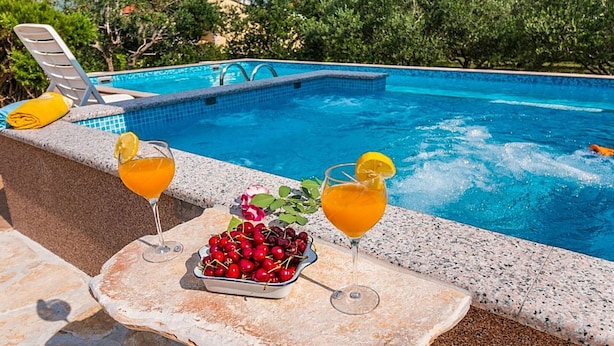 A poolside setting with two drinks, a bowl of cherries, and a glass of wine on a stone table. - Beautiful private villa for 10 guests with private pool, A/C, WIFI, TV, terrace and pets allowed (Solin)