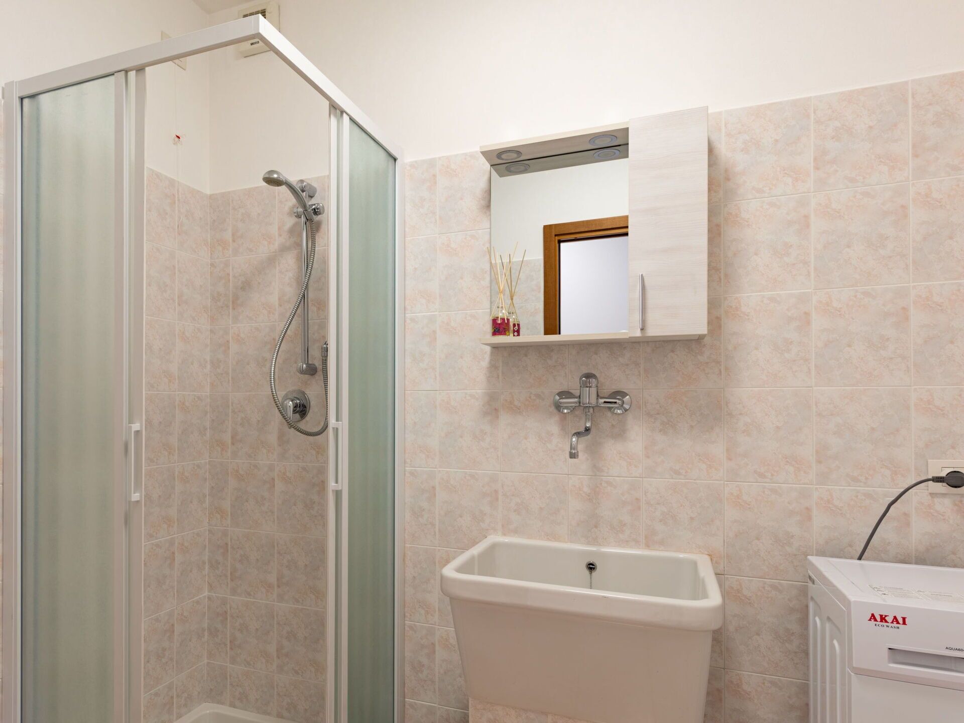 Een badkamer met een douchecabine van glas, een wastafel en een spiegel erboven.