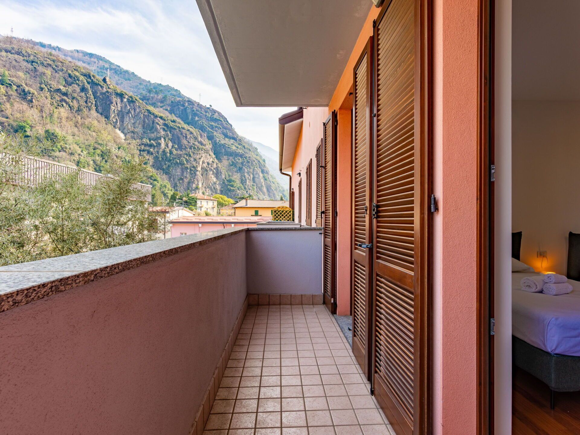 A balcony with a tiled floor, wooden shutters, and a bed with a white bedspread.
