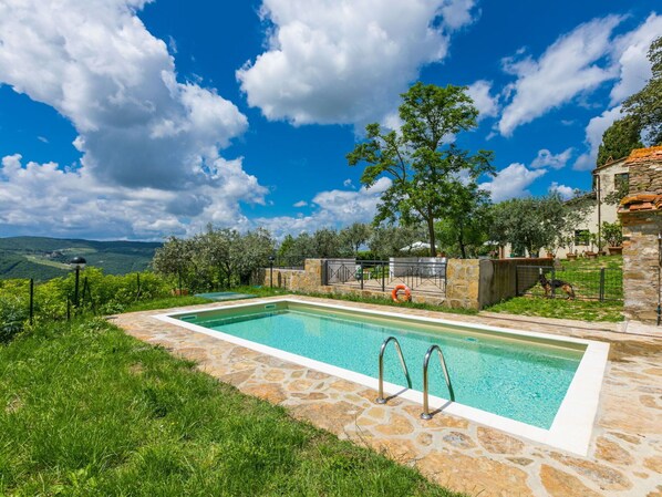 Une piscine rectangulaire bordée de pierres, entourée d’un mur de pierres et d’une végétation luxuriante.