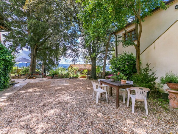 A patio with a table and chairs, surrounded by potted plants and trees.