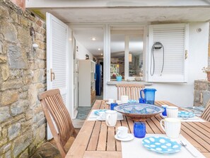 A wooden table set with plates, cups, and a pitcher, with a stone wall and a door on one side.