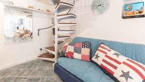 A spiral staircase in a living room with a blue sofa and American flag-themed pillows. - Cosy apartment for 6 people with pool, WIFI, TV, terrace and pets allowed (Castiglione Della Pescaia)