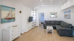 A modern living room with a grey sectional sofa, a flat-screen TV mounted on the wall, and a painting of a sailboat on the wall. - Gorgeous home in Novalja (Novalja)