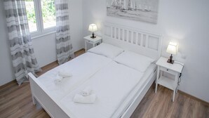 A neatly made bed with white linens and two towels, two bedside tables with lamps, a window with curtains, and a painting of sailboats on the wall. - Gorgeous home in Novalja (Novalja)