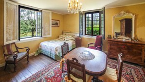 A room with a bed, a chair, a table, a dresser, and a mirror.
