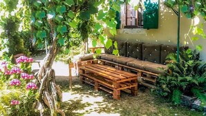 A rustic outdoor seating area with a wooden bench and a cushioned sofa under a vine-covered pergola.