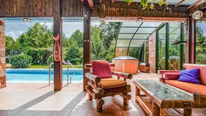 Une terrasse en bois avec un espace clos par des parois de verre, une piscine et du mobilier d’extérieur.