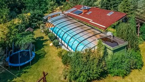Une grande maison moderne dotée d’une piscine intérieure à parois de verre, entourée d’une végétation luxuriante.
